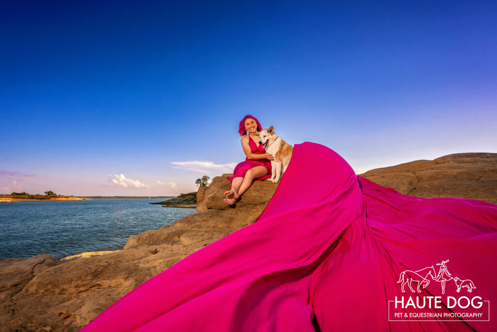 Woman sits on the bluffs of Grapevine Lake while her pink flying dress wraps around her and her dog.