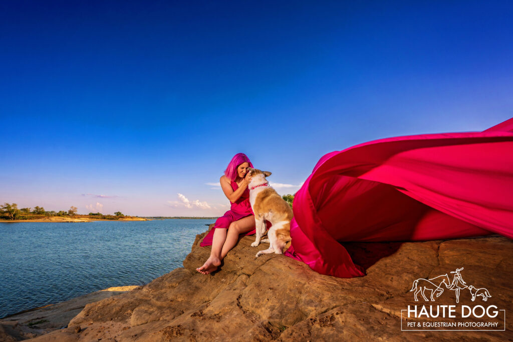 Woman kisses her dog along the edge of Grapevine Lake during her flying dress photoshoot.