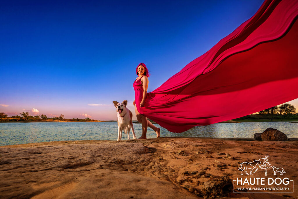 Woman walks along Grapevine Lake with her dog while her pink flying dress floats in the air.