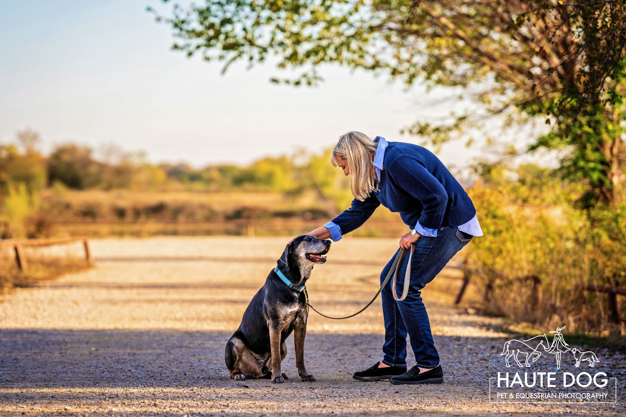 Woman bends down to pat her dog on the head while walking on a trail at Grapevine Lake.