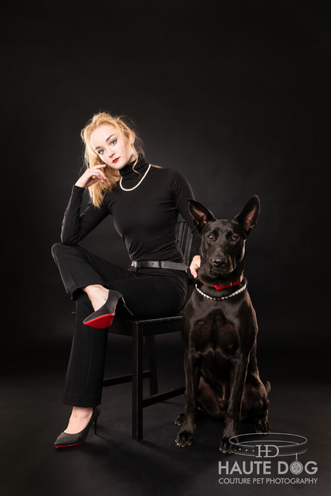 Dog mom wearing all black poses next to her black shepherd on a black background.