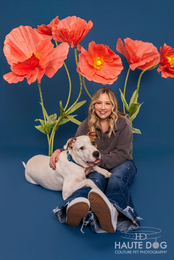 Woman snuggling pit bull on a blue studio backdrop with giant pink flowers around her.